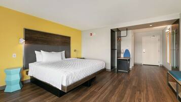 Een moderne hotelkamer met een houten vloer, een bed met wit beddengoed, een klein bijzettafeltje en een bankje.