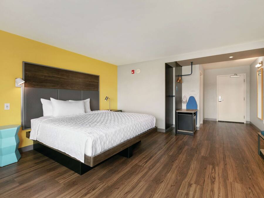 Een moderne hotelkamer met een houten vloer, een bed met wit beddengoed, een klein bijzettafeltje en een bankje.