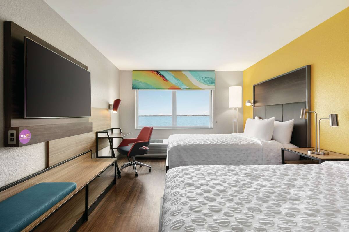 Habitación de hotel con dos camas, un escritorio, una silla, un televisor y una ventana con vistas.