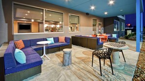 A modern outdoor seating area with a sofa, round table, and chairs, featuring large windows and a view of the cityscape. - Tru by Hilton Wytheville (Wytheville)