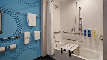 A bathroom with a blue wall, white fixtures, a bathtub with grab bars, a shower with a handheld showerhead, and a towel rack with towels.