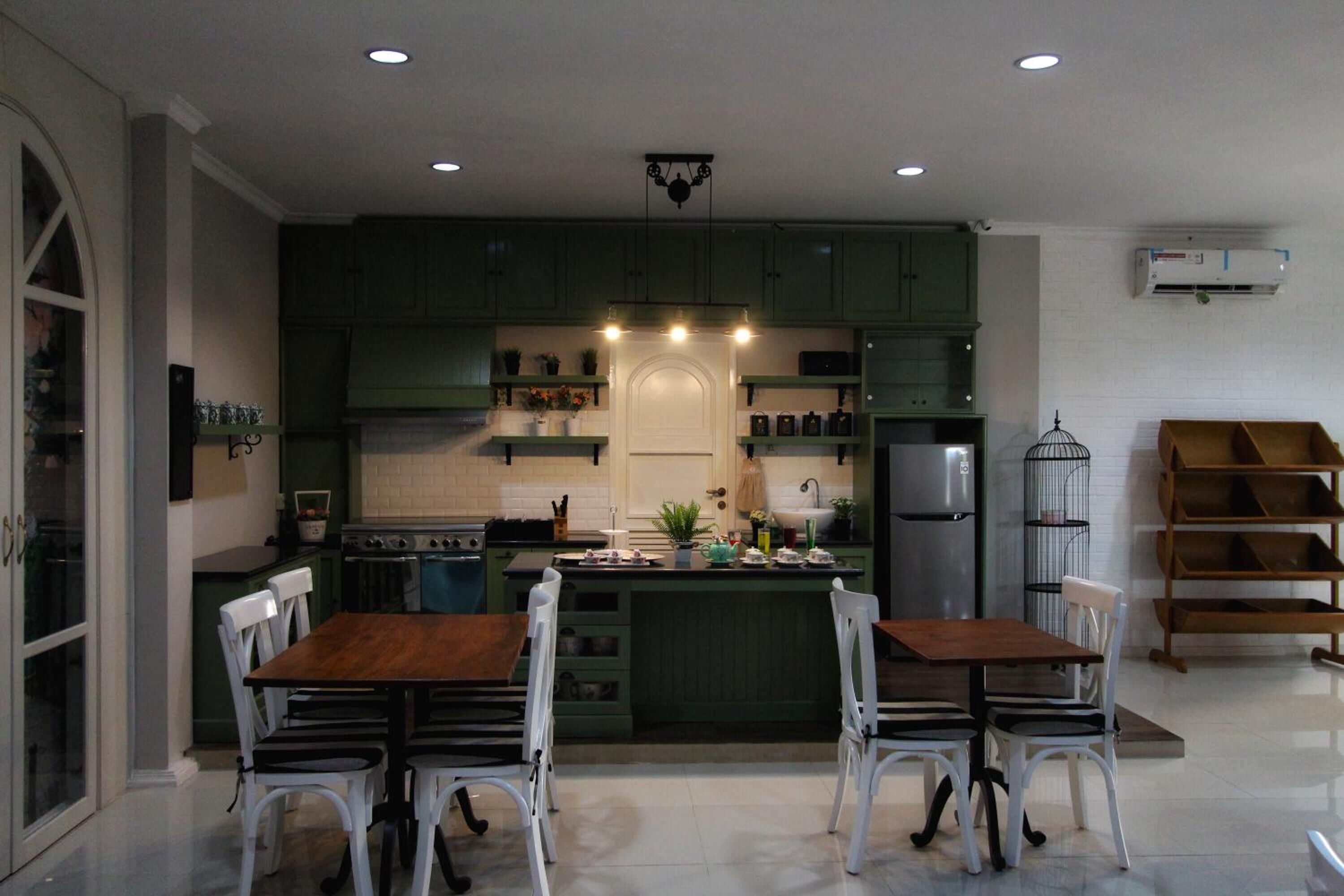 A modern kitchen with green cabinets, a central island, white chairs, and a built-in oven.