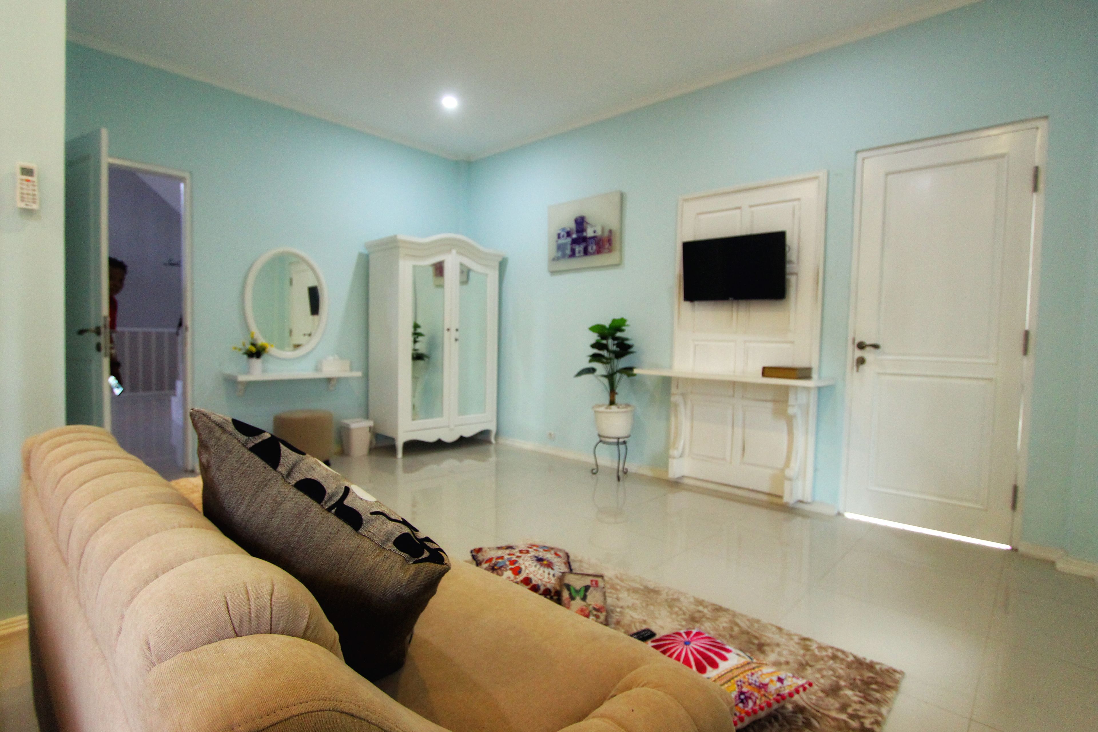 A living room with a beige sofa, a white cabinet, a television on the wall, and a door.