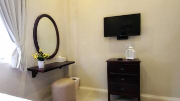 Un dormitorio con cama, mesita de noche con espejo, cómoda, televisor montado en la pared y ventana con cortinas.