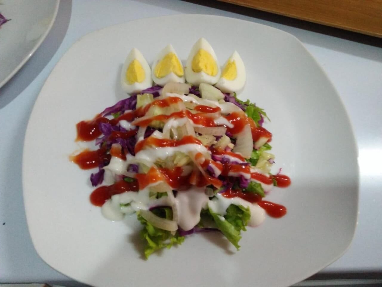 A white plate with a salad topped with boiled eggs, red cabbage, and a white dressing.