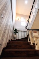 Una escalera de madera con balaustres blancos, una planta en maceta y un letrero que indica un baño.
