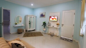 A living room with a sofa, a television, a cabinet, a mirror, and a door. - Omah Madam Bed & Breakfast (Semarang)