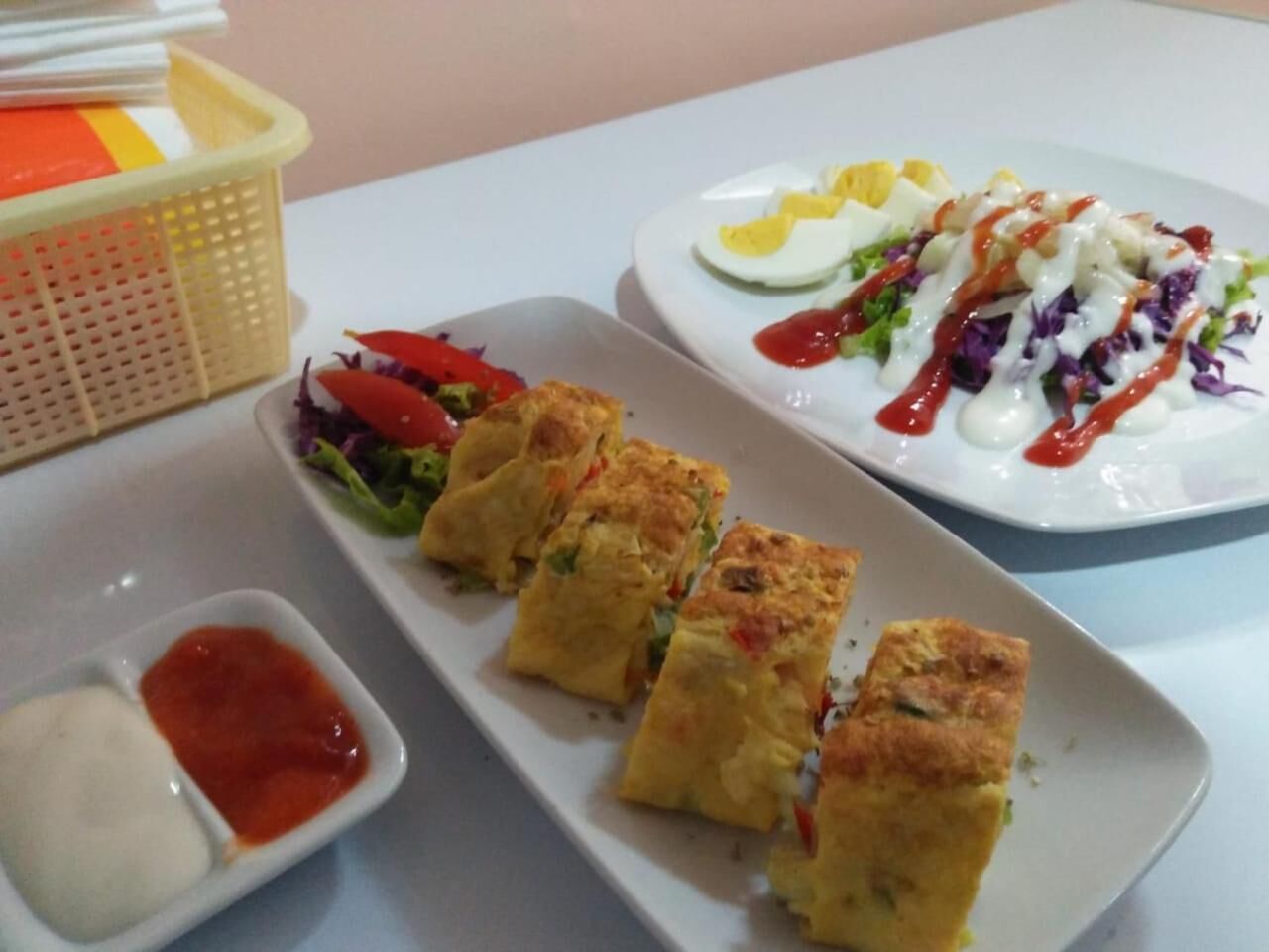 A table with a variety of dishes including a salad, a plate with eggs and a creamy sauce, and a dish with a red sauce.