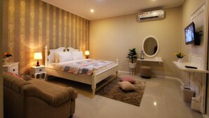 A bedroom with a bed, bedside tables, a TV, a mirror, a plant, and a bathroom area with a toilet and sink. - Omah Madam Bed & Breakfast (Semarang)