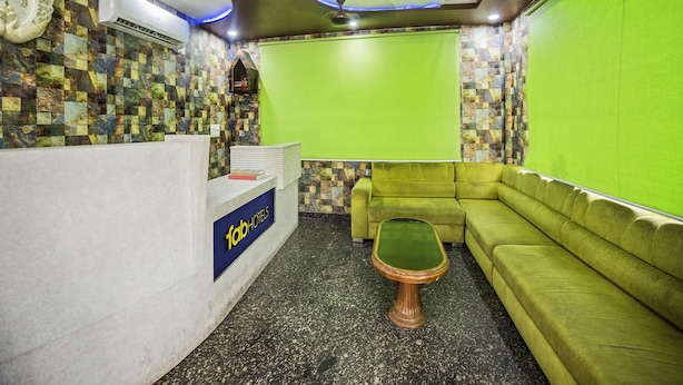 A hotel reception area with a green screen, a wooden coffee table, a green sofa, and a clock on the wall.