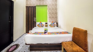 A hotel room with a bed, a green door, a patterned wall, and a brown chair.