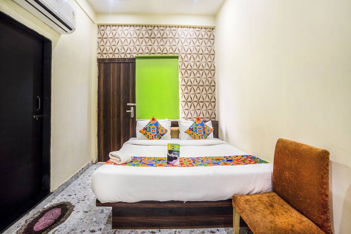 A hotel room with a bed, a green door, a patterned wall, and a brown chair.