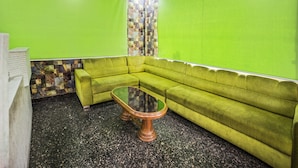 A green room with a sectional sofa, a glass coffee table, and a patterned wall.
