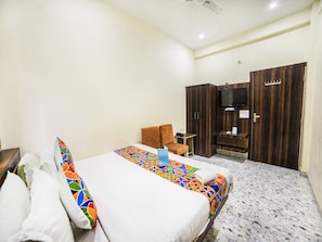 A hotel room with a bed, a chair, a wardrobe, and a television. - FabHotel Glorify Stay (Mathura)
