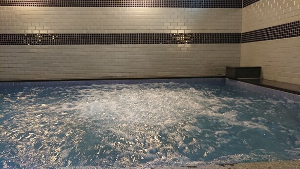 A hot tub with bubbling water, surrounded by white tiled walls and a black tiled border. - Green Rich Hotel & Capsule Naha Artificial Hot Spring Futamata Yunohana (Naha)