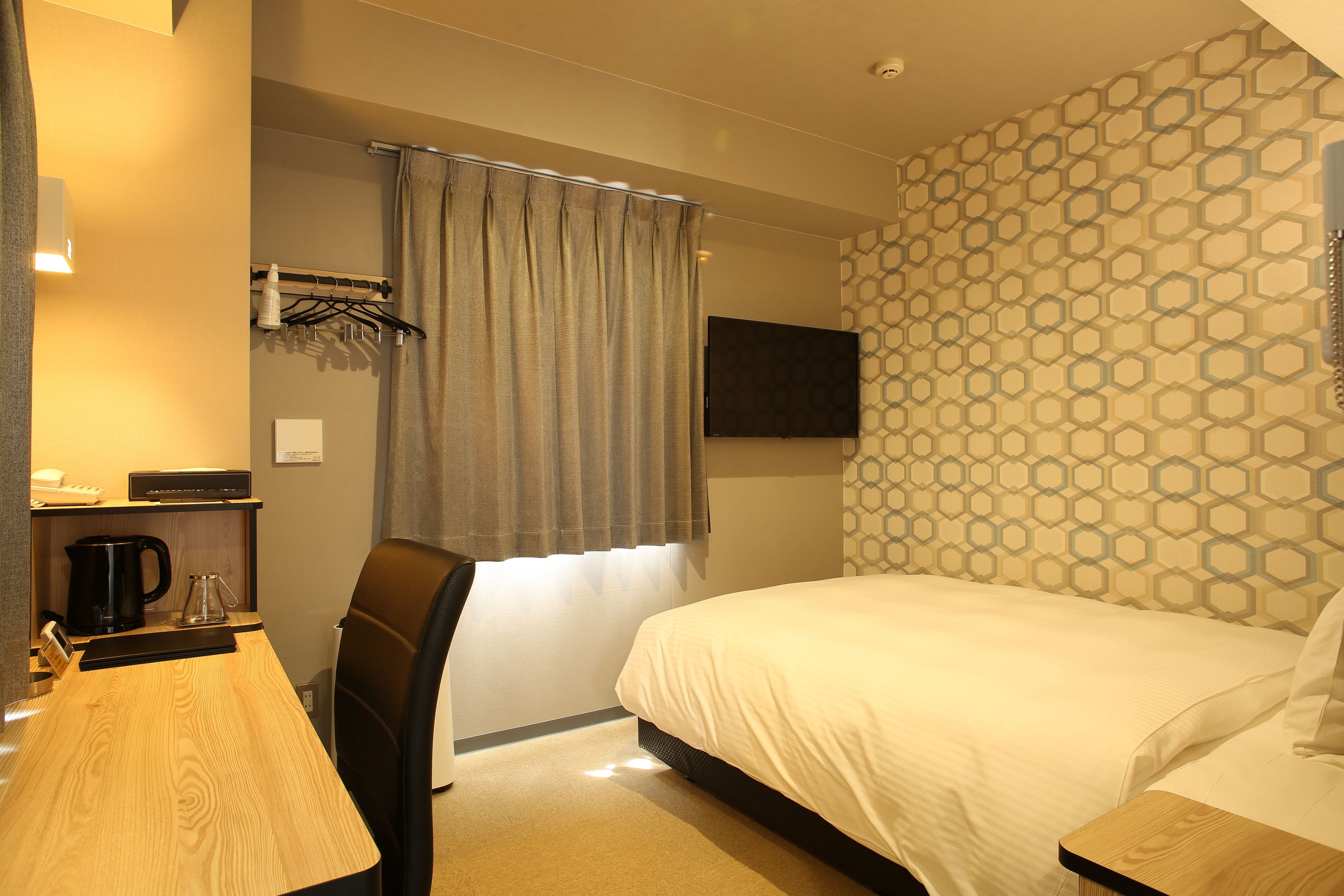 Une chambre d’hôtel avec un lit, un bureau doté d’une bouilloire, une chaise et un rideau de douche.