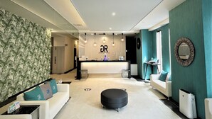 A modern hotel lobby with a reception desk, seating area, and a large mirror on the right wall. - Green Rich Hotel & Capsule Naha Artificial Hot Spring Futamata Yunohana (Naha)