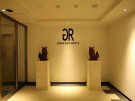 Un vestíbulo con mostrador de recepción, dos estatuas decorativas de animales y un letrero de Green Rich Hotels.