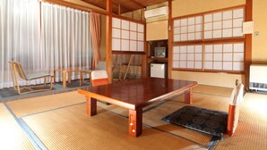 A tatami mat room with a low wooden table, two chairs, a small TV, and a traditional Japanese air conditioning unit. - Hatsunoyu hotel (Yamanouchi)