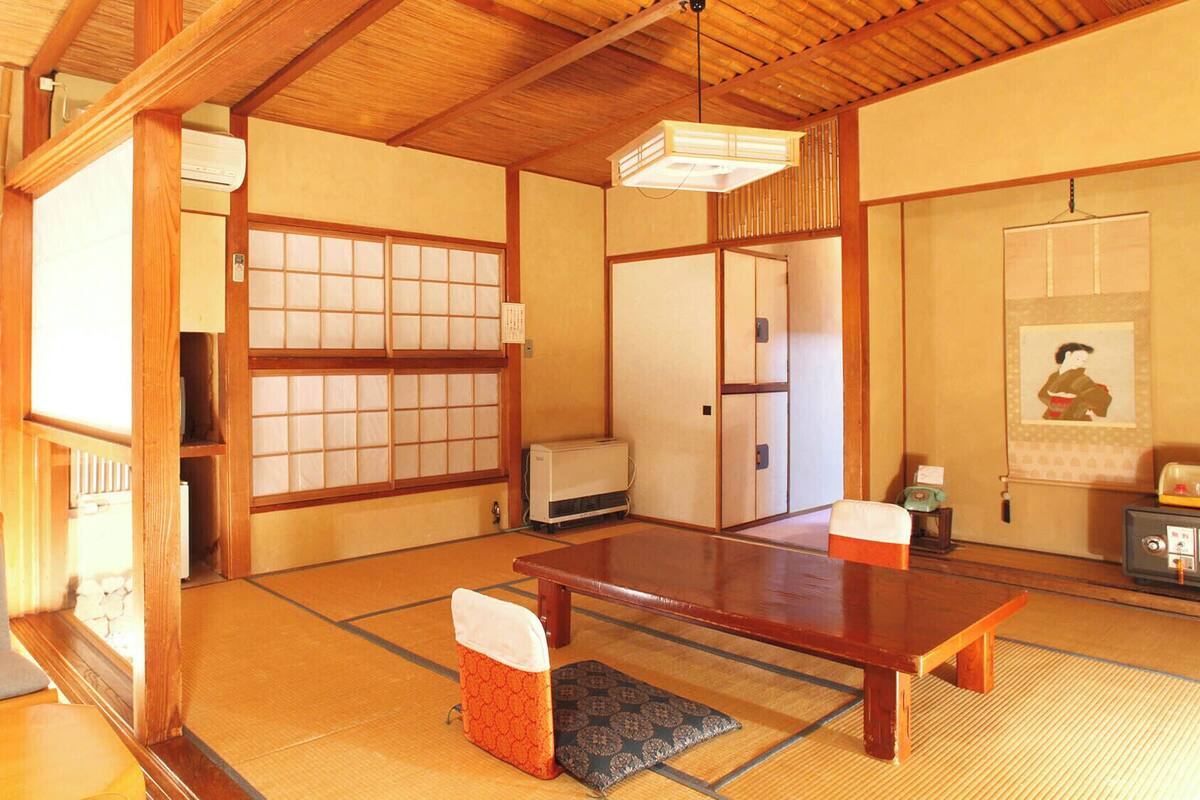 Ein traditioneller japanischer Raum mit Tatami-Böden, einem niedrigen Holztisch, Schiebetüren und einer hängenden Leuchte.