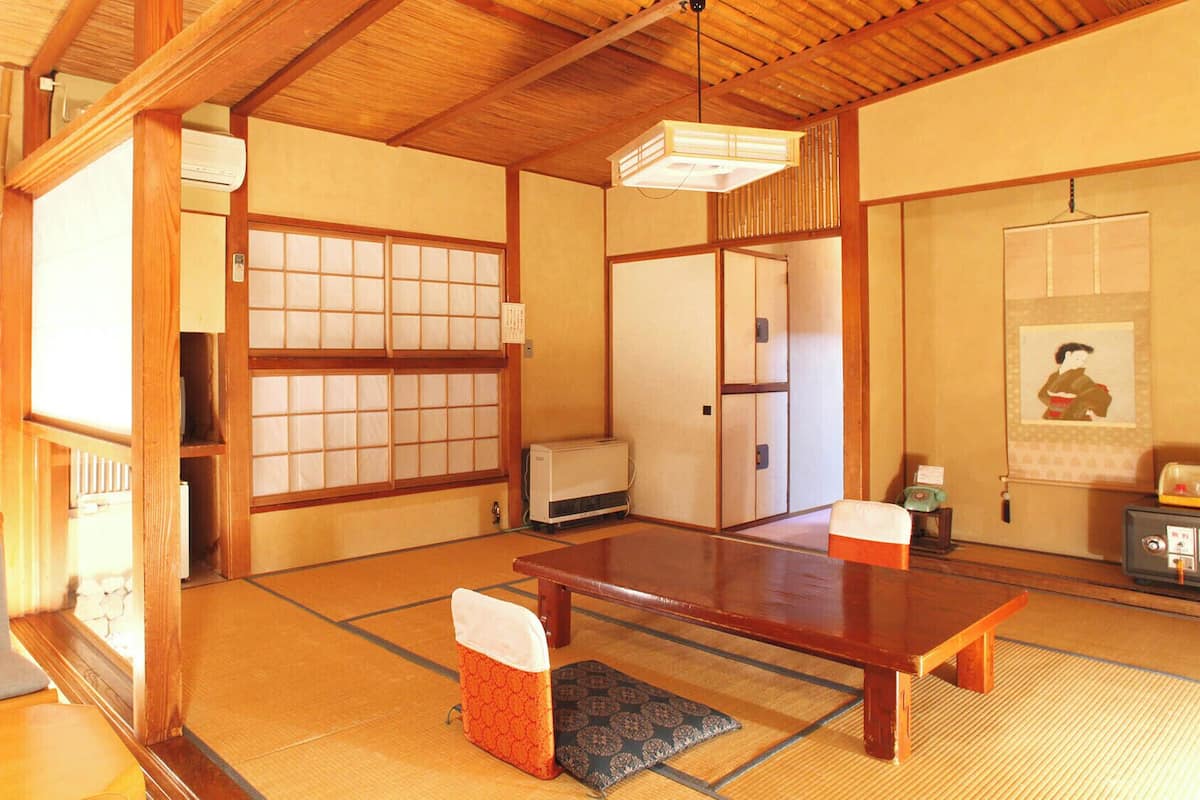 Una habitación japonesa tradicional con suelo de tatami, una mesa de madera baja, puertas correderas y una lámpara colgante.