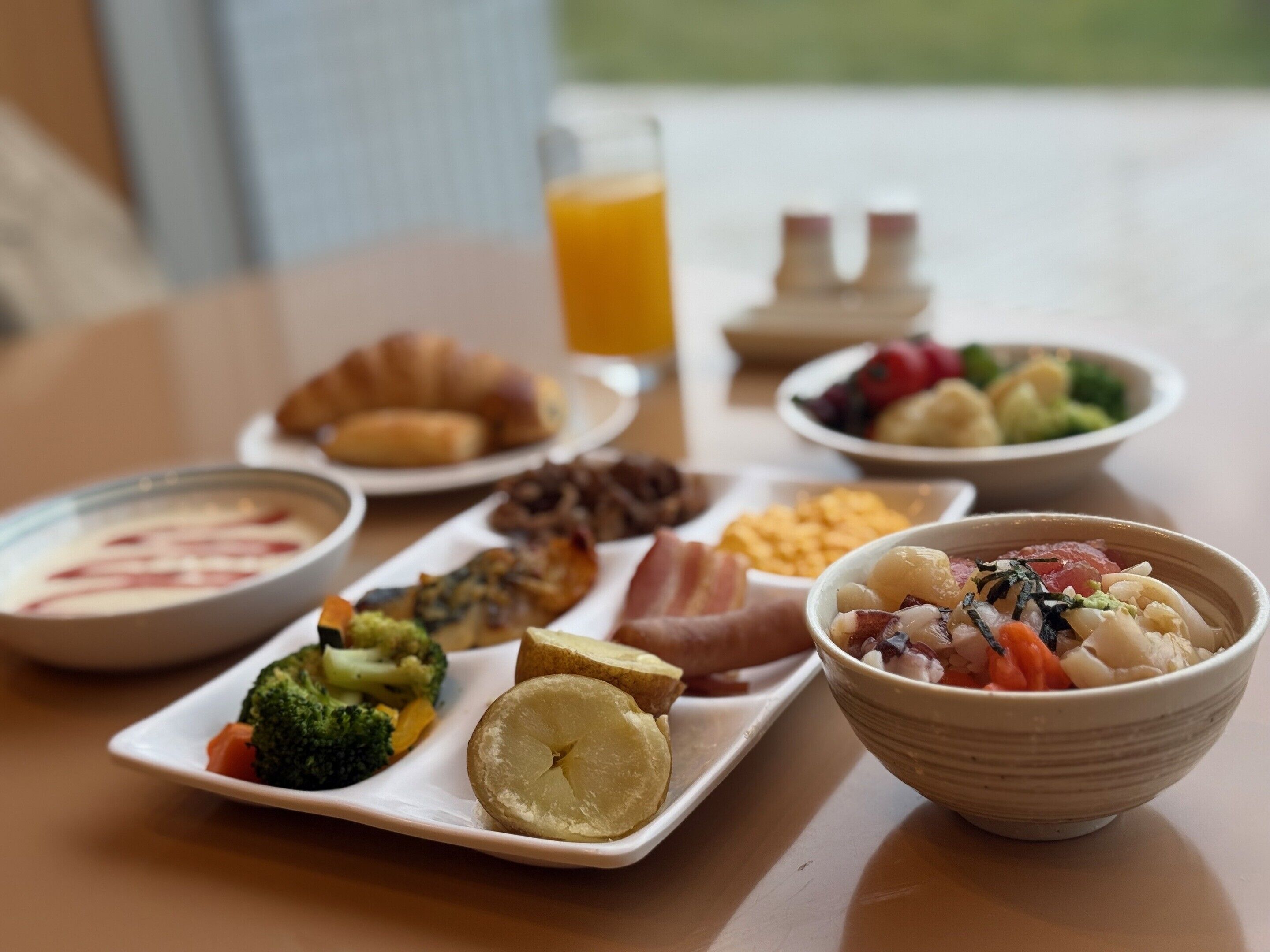 Ein Frühstückstisch mit verschiedenen Speisen, darunter Croissants, eine Suppenschüssel und eine Gemüseplatte.