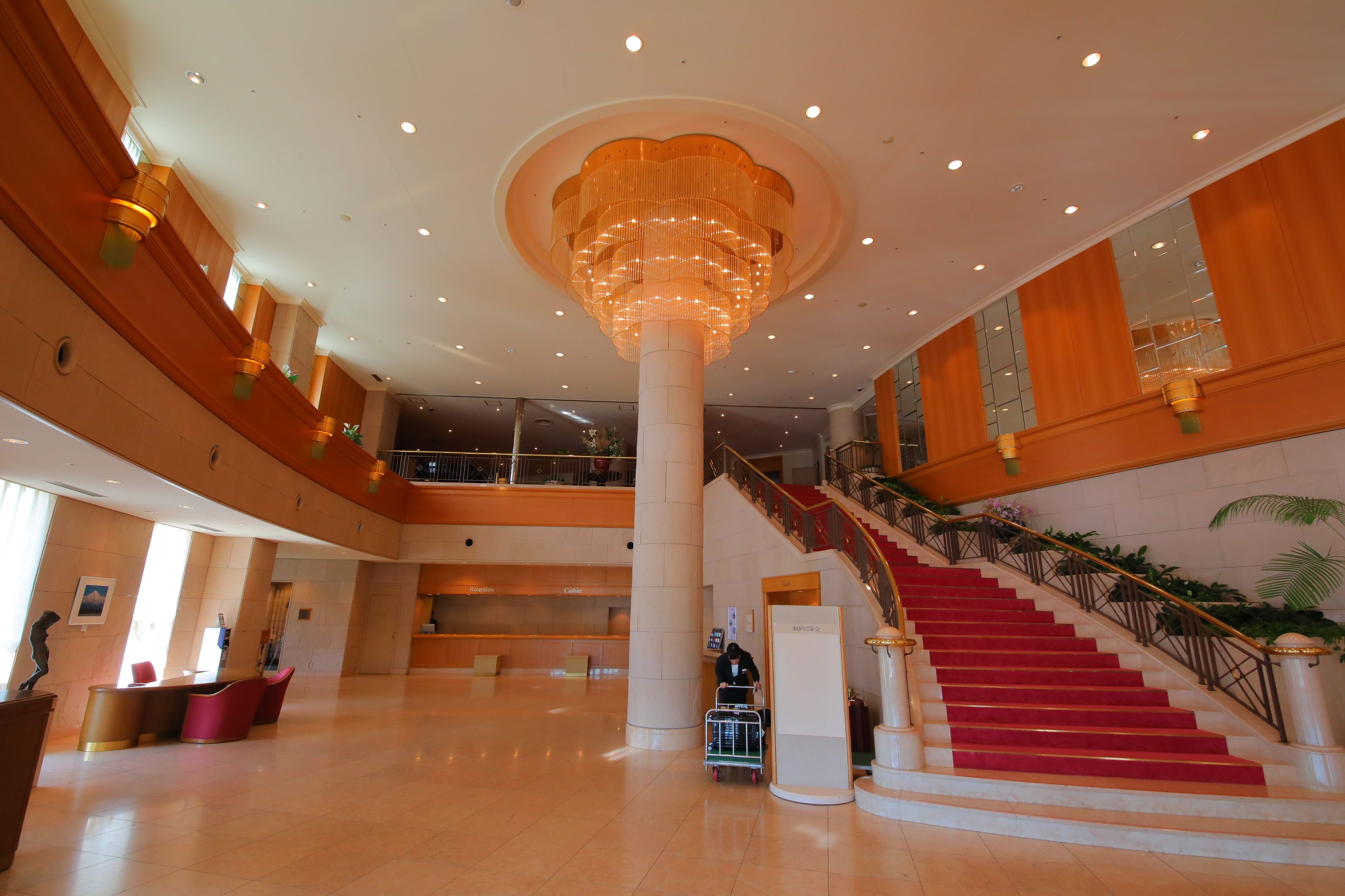 A spacious lobby with a grand chandelier, a staircase with red carpet, and a reception desk.