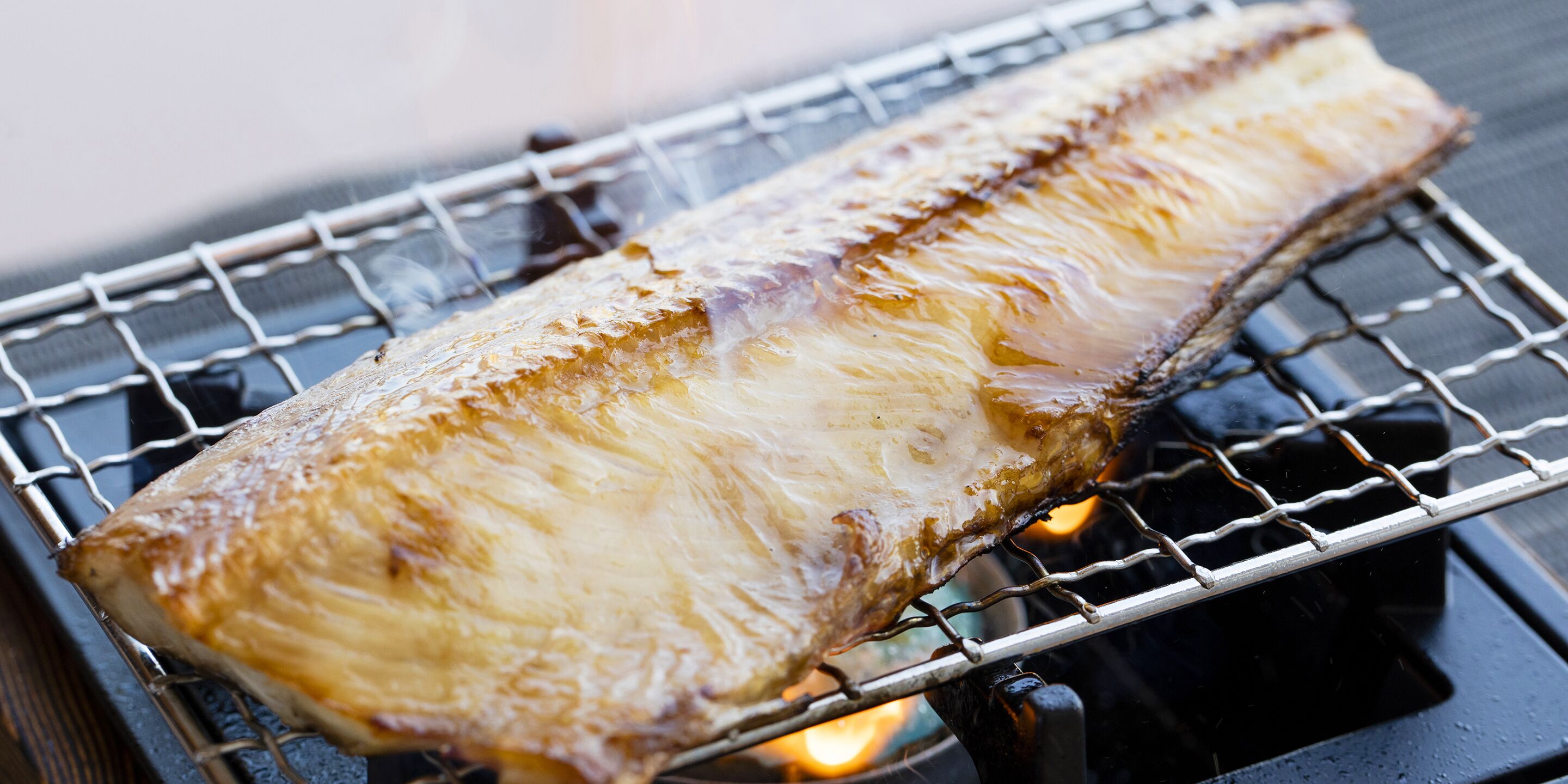 A fish being grilled on a metal rack over an open flame.