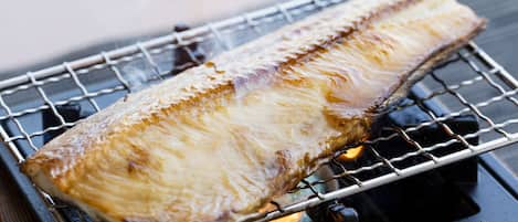 A fish being grilled on a metal rack over an open flame.