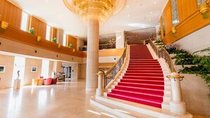Een statig hotel ontvangsthal met een rode tapijstvloer, marmeren zuilen en een grote kroonluchter.