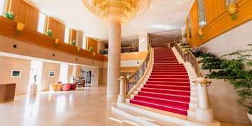 Un lobby de hotel imponente con alfombra roja, columnas de mármol y un gran candelabro.