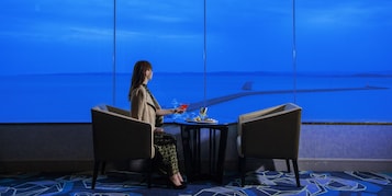 Una mujer sentada a una mesa con vista al mar y un velero.