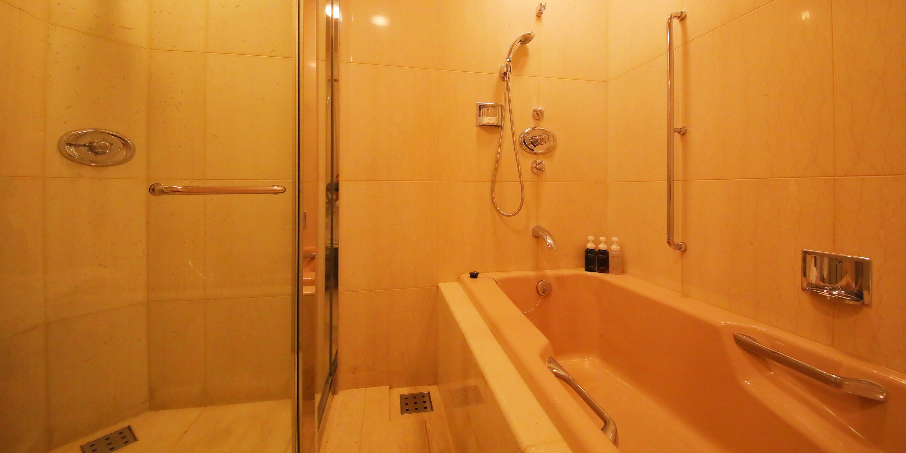 A bathroom with a glass shower enclosure, a bathtub with a handheld showerhead, and a wall-mounted faucet.