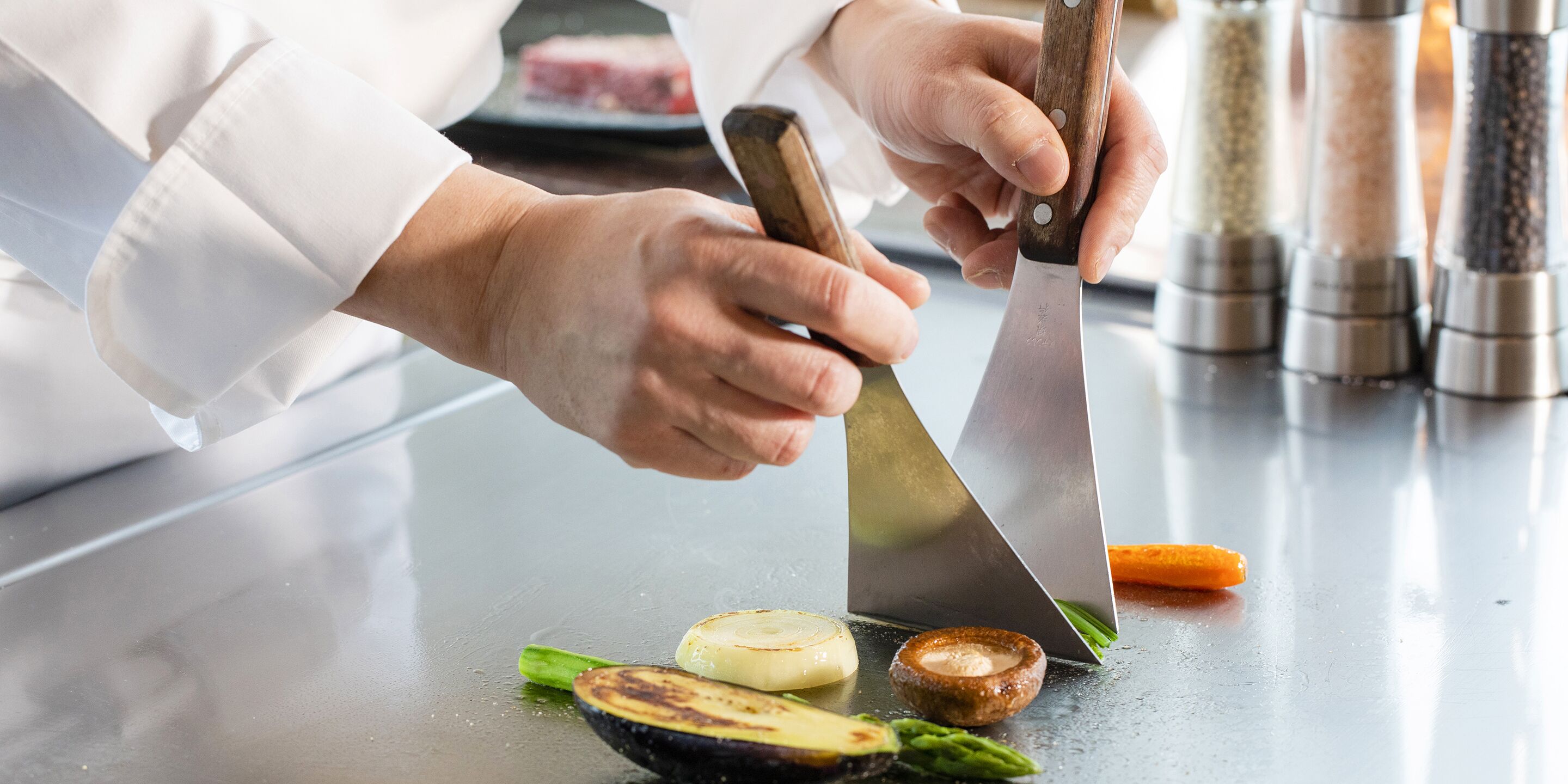 Un chef cortando verduras con un cuchillo grande sobre una encimera de cocina.