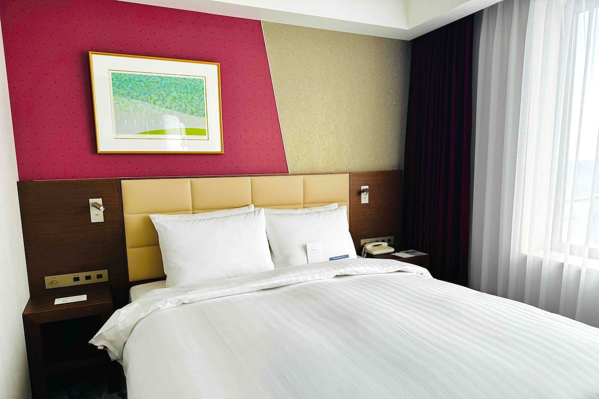 Ein Hotelzimmer mit Bett, Nachttisch, Telefon und einem Gemälde an der Wand.