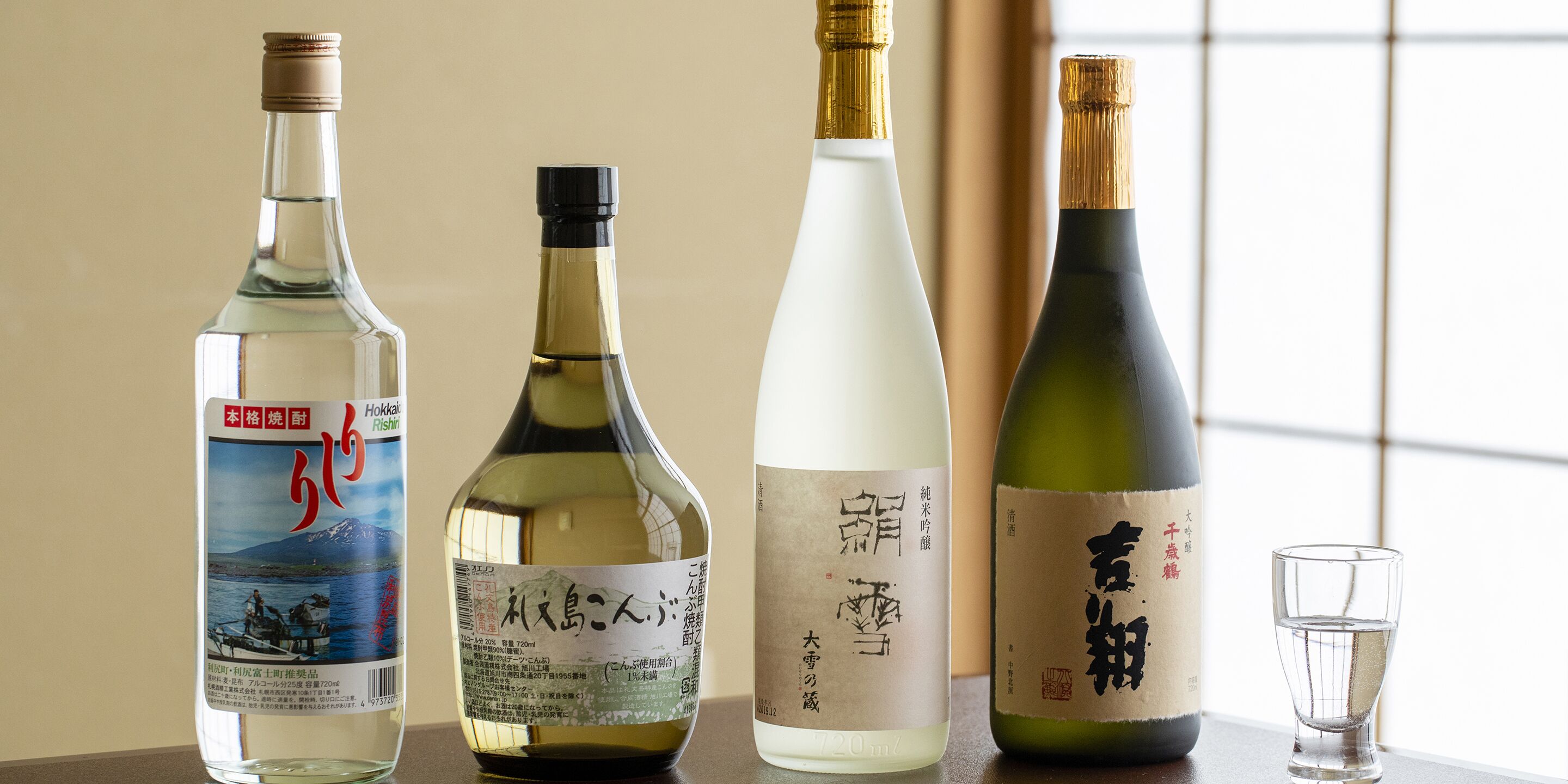Four bottles of Japanese sake on a table with a glass of water.