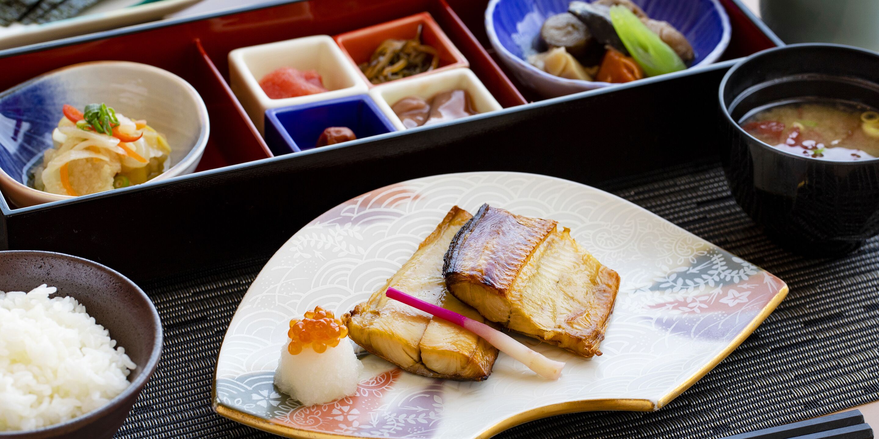 A traditional Japanese meal with rice, fish, and pickled vegetables on a patterned plate.