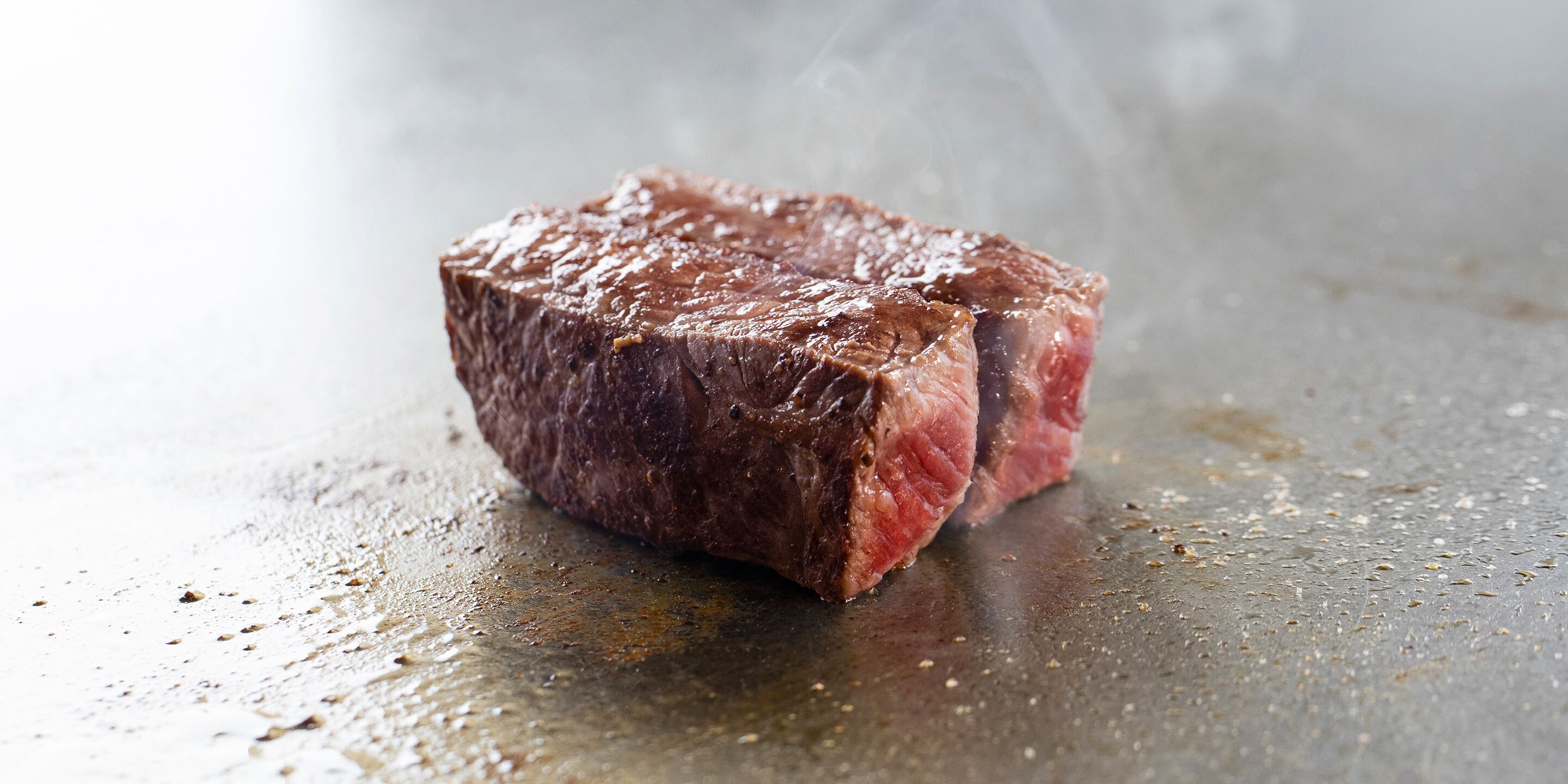 A steak on a grill with visible grill marks and some smoke.