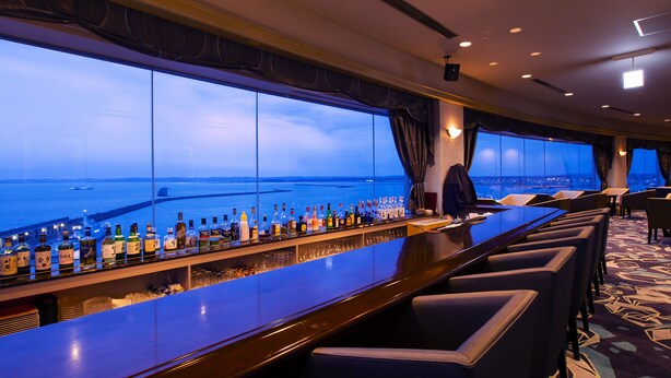 Een bar met uitzicht op zee, barstoelen en een gekleurd tapijt.