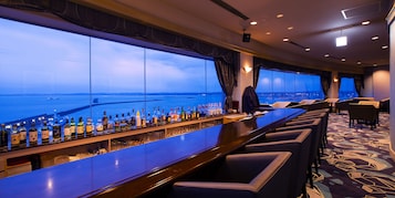 Un bar con vistas al mar, taburetes y una alfombra estampada.