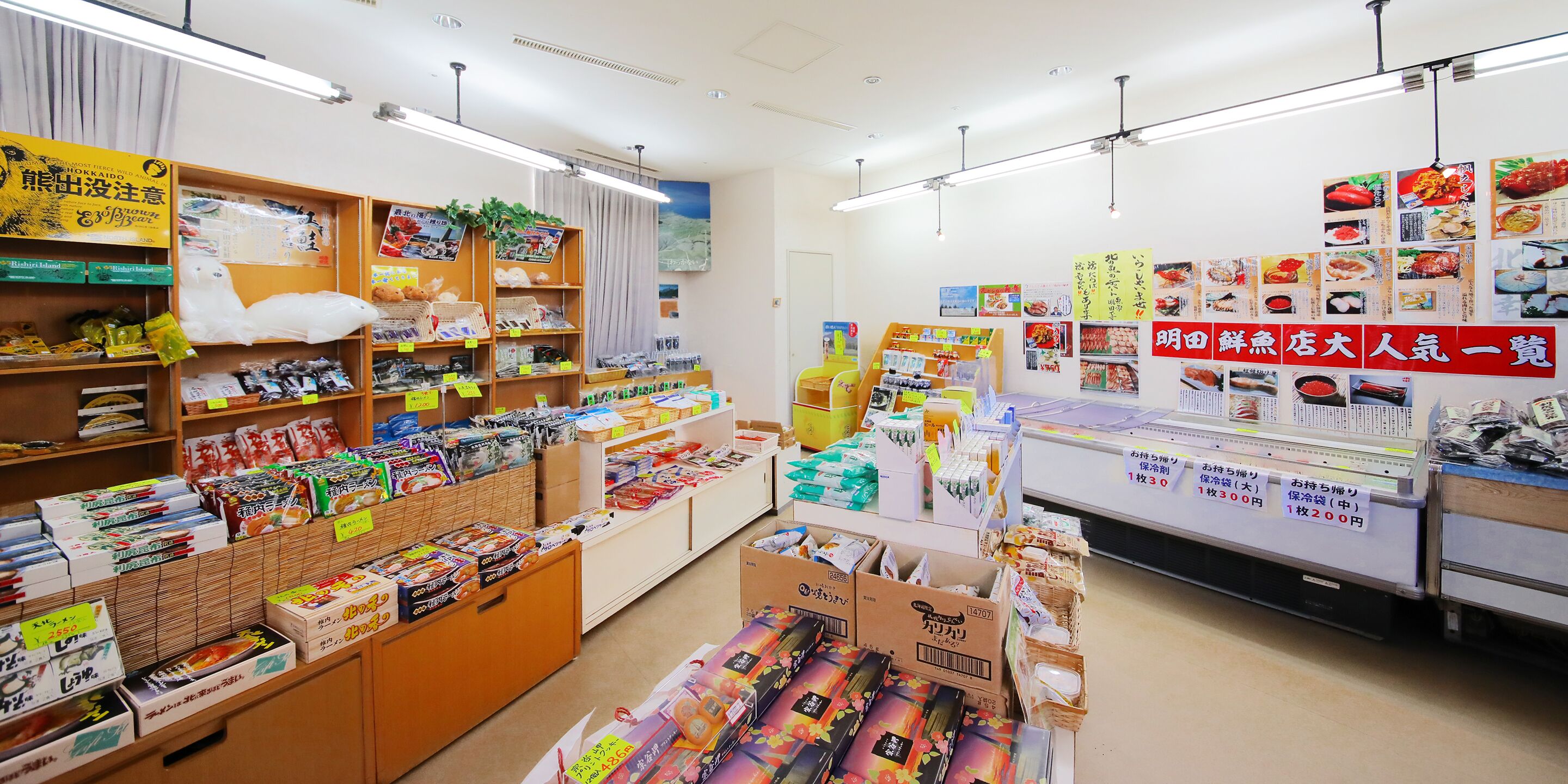 A store with shelves stocked with various packaged goods, a display counter with promotional materials, and signs indicating prices.