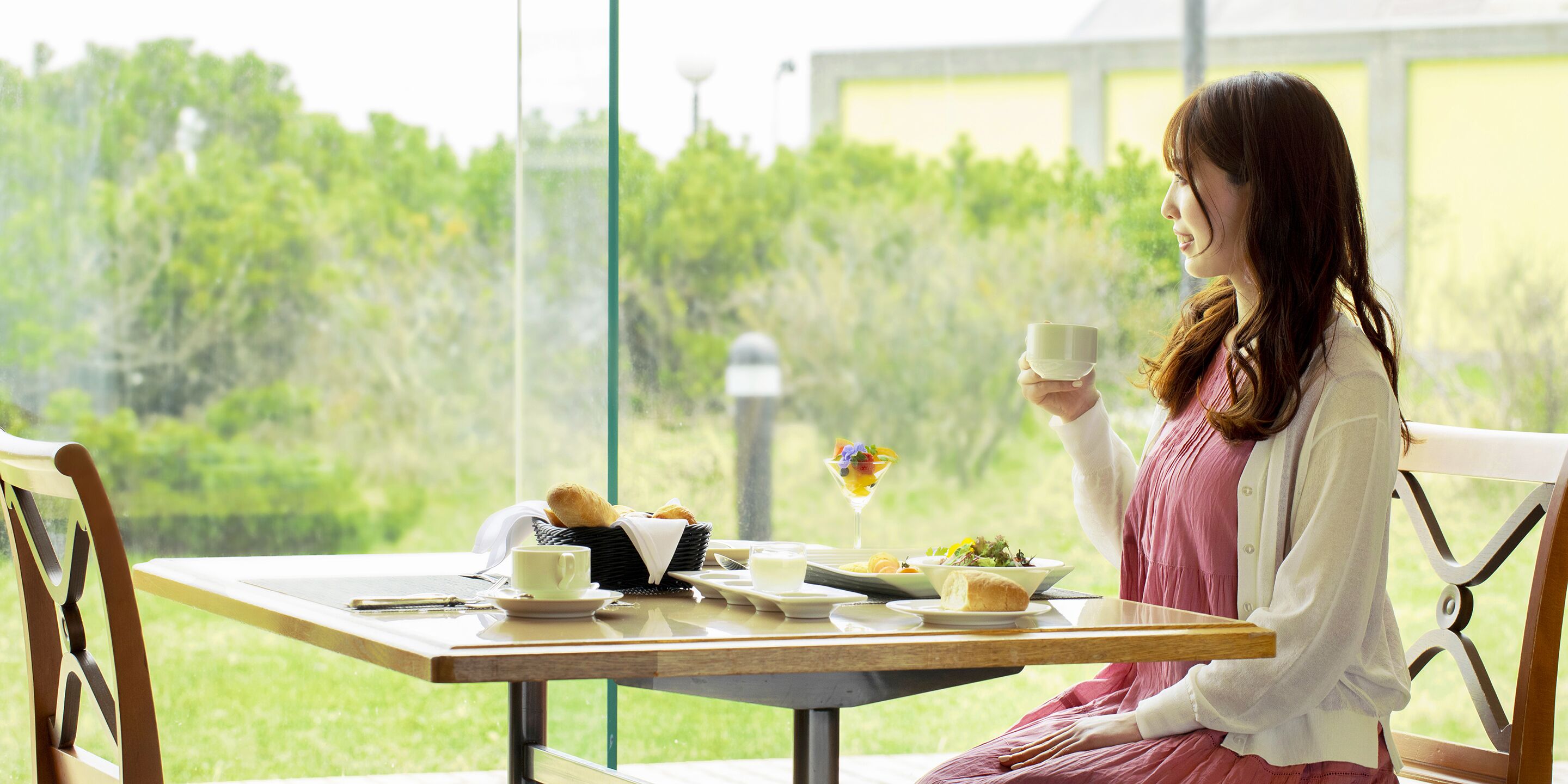 A dining table with a meal, a cup, and a basket of bread.