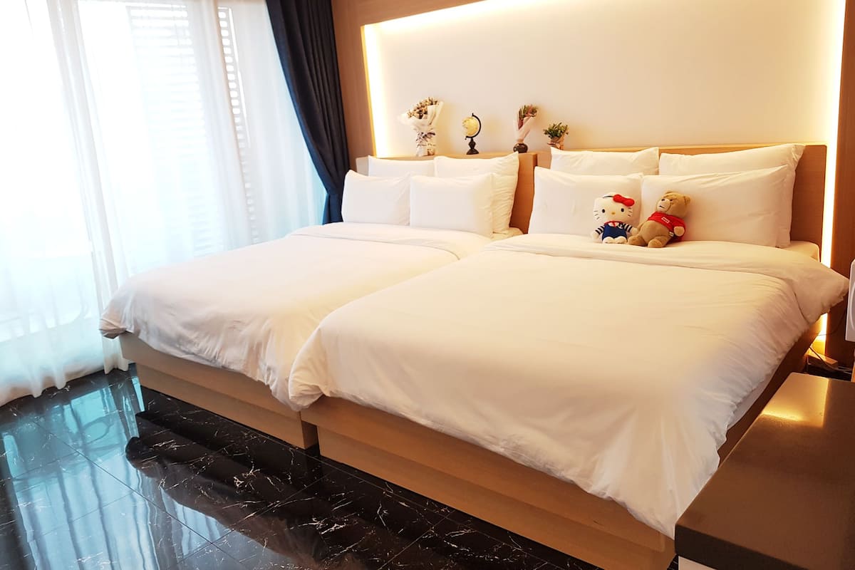 Ein Doppelbett mit weißen Leinen, ein Nachttisch, eine Lampe, ein Teddybär und ein Hello Kitty Plüschtier.