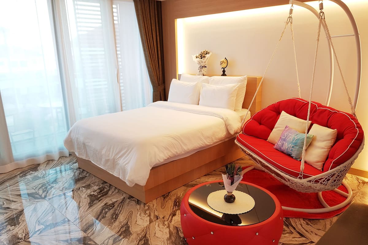 Ein modernes Hotelzimmer mit einem großen Bett, einem roten Hängesessel und einem kleinen runden Tisch.