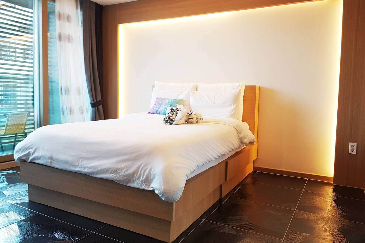 Ein modernes Schlafzimmer mit einem großen Bett, einem Holzkopfende und Blick ins Freie durch ein großes Fenster.