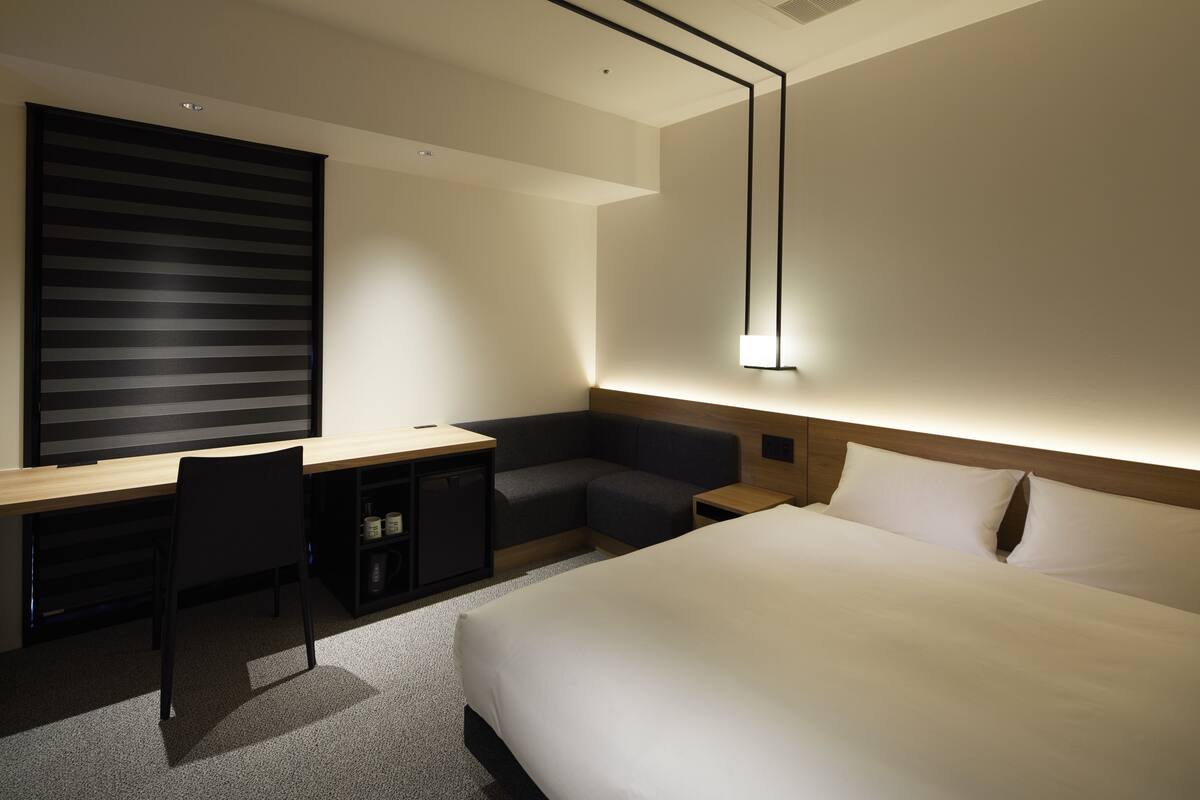 Een moderne hotelkamer met een groot bed, een bureau met stoel, een zithoekje en een nachtkastje.