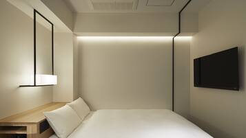 Une chambre d’hôtel moderne avec un lit bien fait, une table de chevet en bois sur laquelle reposent deux tasses, un téléviseur fixé au mur et un luminaire au plafond.