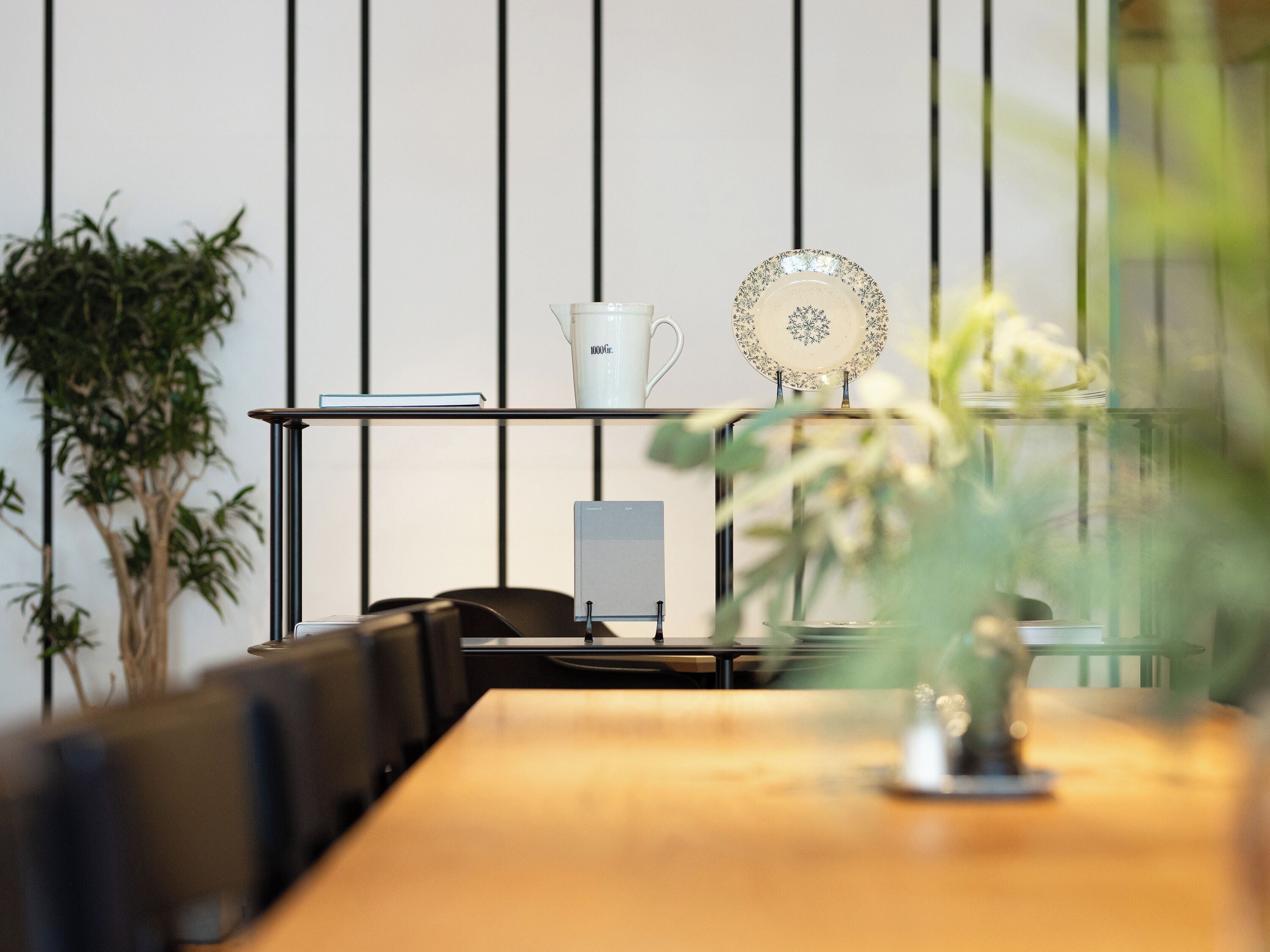 A modern conference room with a wooden table, black chairs, a glass table with a white mug and a decorative plate, and a potted plant.