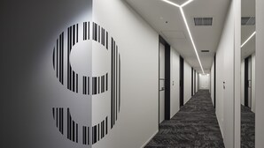 Ein moderner Hotelkorridor mit geometrischem Wanddesign, einem gemusterten Teppich und einer langen, geraden Diele.