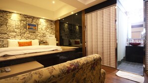 Habitació d'hotel moderna amb paret de pedra, un llit gran, un sofà i un bany amb cortina de bany amb un disseny decoratiu.